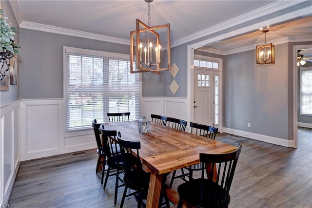 dining space featuring a decorative wall, a notable chandelier, dark wood-style flooring, wainscoting, and crown molding