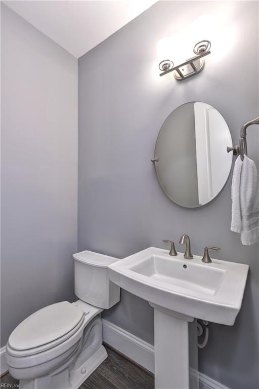 half bathroom with wood finished floors, toilet, and baseboards