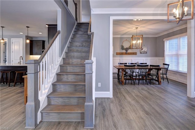 stairway with a chandelier, wainscoting, crown molding, and wood finished floors