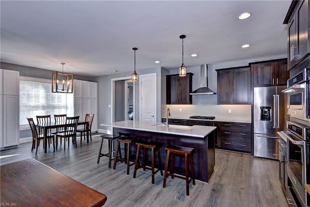 kitchen with a breakfast bar, stainless steel appliances, light countertops, wall chimney range hood, and a sink