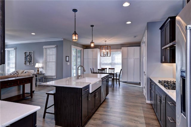 kitchen with a breakfast bar area, under cabinet range hood, a sink, light countertops, and appliances with stainless steel finishes