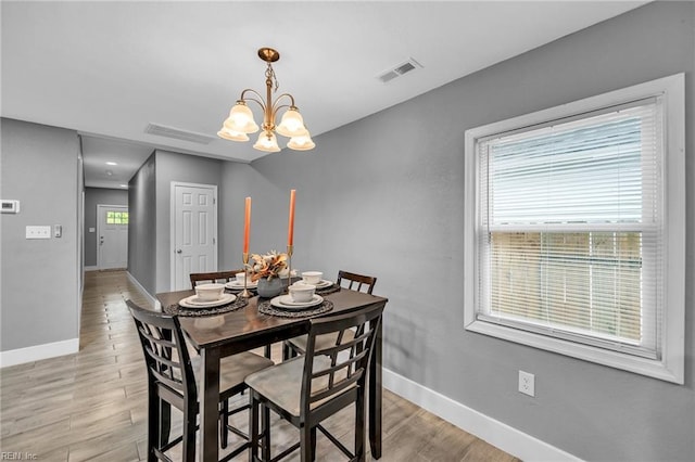 dining space featuring light wood finished floors, an inviting chandelier, visible vents, and baseboards