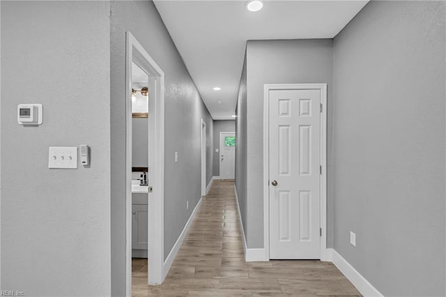 hallway featuring light wood-type flooring, baseboards, and recessed lighting