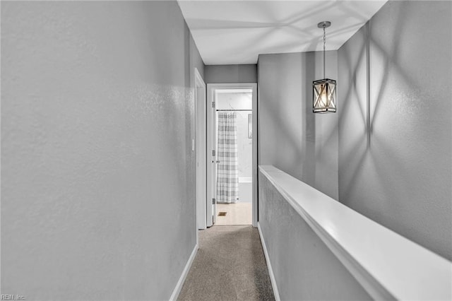 hall featuring a textured wall, dark colored carpet, and baseboards