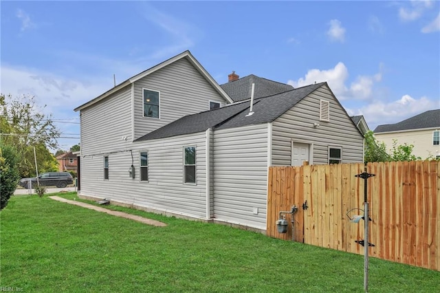 view of side of home with roof with shingles, a chimney, fence, and a yard