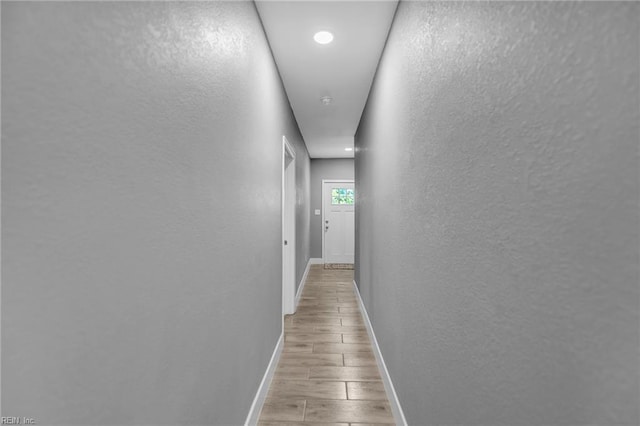 corridor with baseboards, wood finished floors, and a textured wall