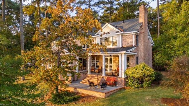 back of house featuring brick siding, a lawn, a chimney, and a patio area