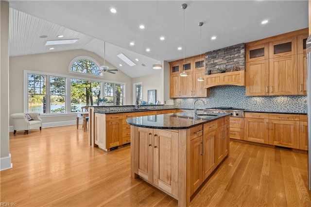 kitchen with dark stone counters, tasteful backsplash, a kitchen island with sink, and light wood-style flooring