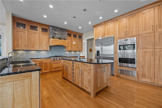 kitchen with light wood finished floors, dark stone counters, appliances with stainless steel finishes, a warming drawer, and a sink