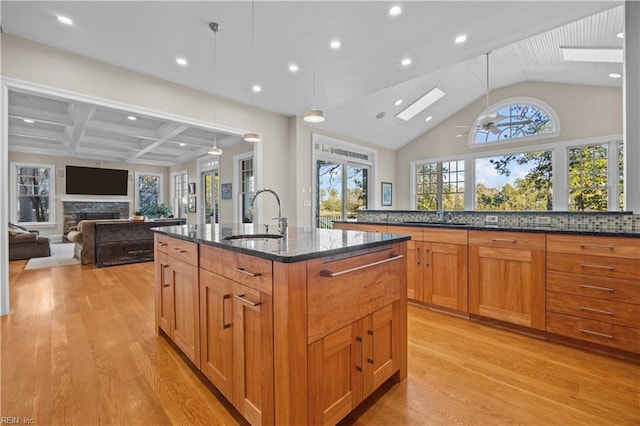 kitchen with a center island with sink, a sink, dark stone counters, a skylight, and a fireplace