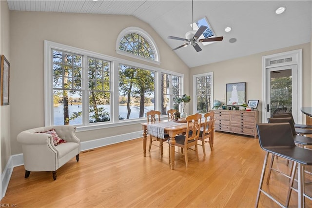 dining space with baseboards, ceiling fan, a water view, light wood-type flooring, and high vaulted ceiling