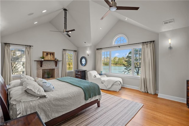 bedroom featuring visible vents, a water view, high vaulted ceiling, light wood-style floors, and baseboards