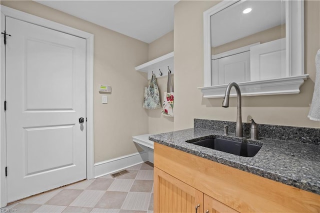 kitchen with a sink, visible vents, baseboards, and dark stone counters