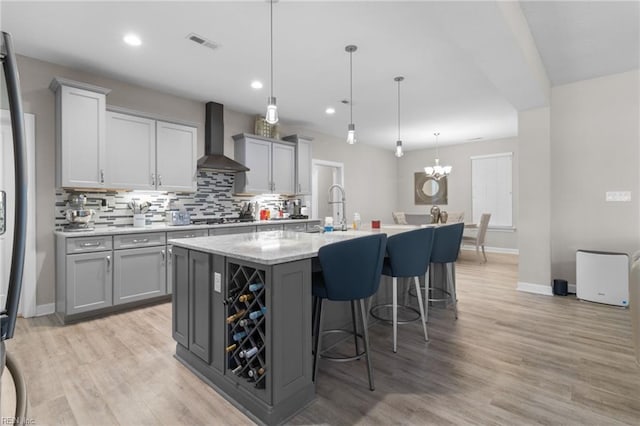 kitchen with tasteful backsplash, gray cabinets, light wood-style flooring, and wall chimney exhaust hood