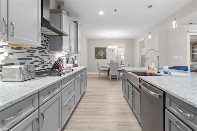 kitchen with stainless steel appliances, a sink, wall chimney range hood, gray cabinets, and tasteful backsplash