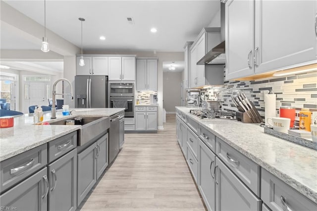 kitchen featuring light wood-style flooring, appliances with stainless steel finishes, light stone counters, gray cabinets, and wall chimney range hood