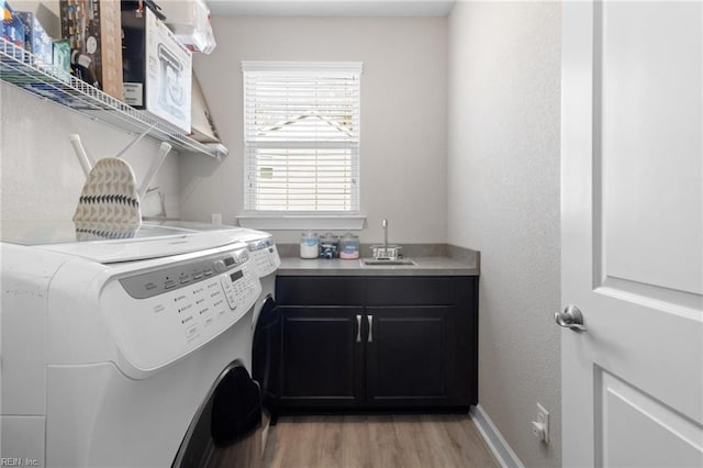 laundry room with light wood finished floors, cabinet space, baseboards, washing machine and clothes dryer, and a sink