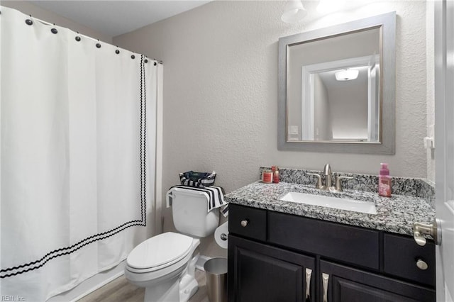 full bathroom featuring curtained shower, a textured wall, toilet, vanity, and wood finished floors