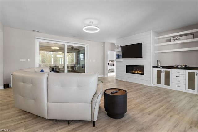 living room featuring a large fireplace, light wood-style flooring, and baseboards