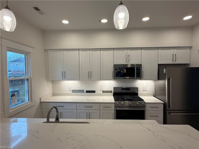 kitchen with appliances with stainless steel finishes, a sink, visible vents, and light stone countertops