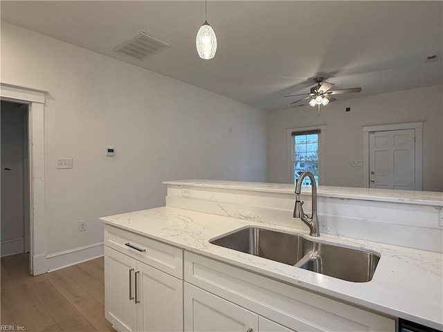 kitchen with visible vents, light wood-style floors, white cabinetry, a sink, and light stone countertops