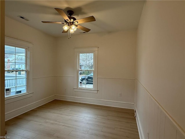 spare room featuring a wainscoted wall, ceiling fan, wood finished floors, and visible vents