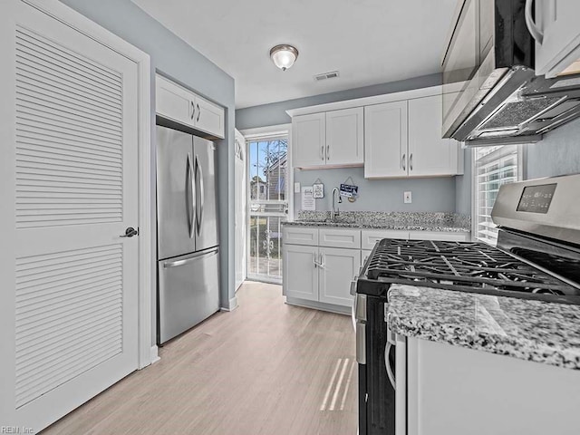 kitchen featuring light stone counters, stainless steel appliances, visible vents, white cabinets, and light wood-type flooring