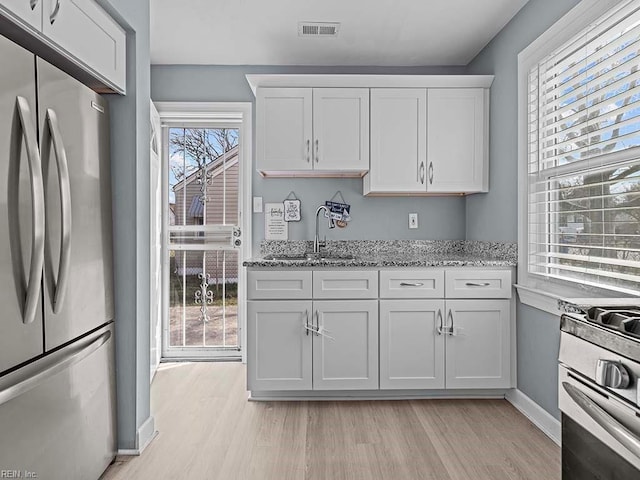 kitchen featuring light wood finished floors, visible vents, light stone counters, stainless steel appliances, and a sink