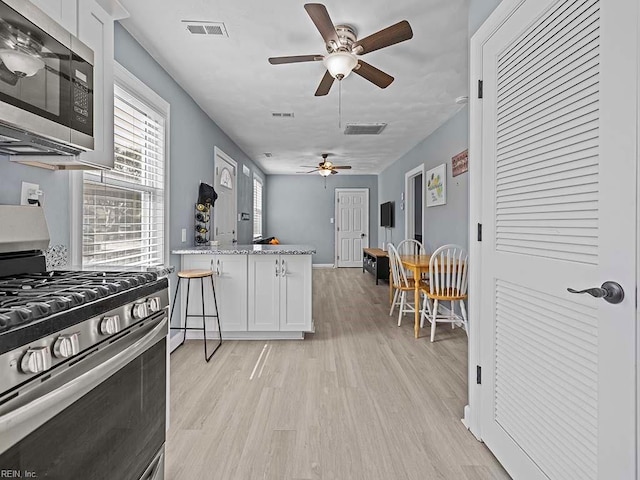 kitchen with a peninsula, visible vents, white cabinets, appliances with stainless steel finishes, and light wood-type flooring