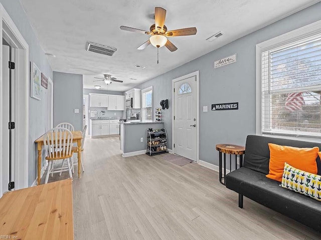 interior space featuring a ceiling fan, light wood-type flooring, visible vents, and baseboards