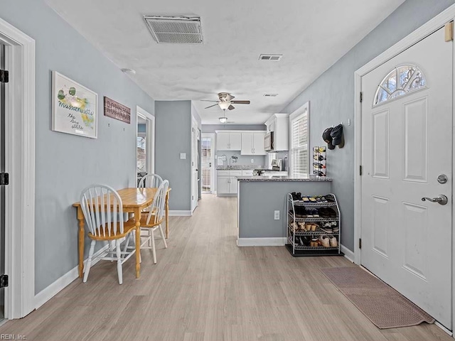 interior space with stainless steel microwave, light wood-type flooring, visible vents, and white cabinets