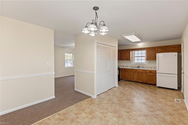 kitchen featuring visible vents, light colored carpet, freestanding refrigerator, hanging light fixtures, and light countertops