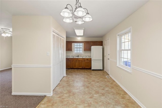 kitchen featuring a sink, baseboards, light countertops, freestanding refrigerator, and brown cabinetry