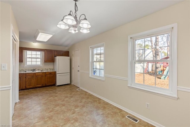 kitchen with light countertops, visible vents, hanging light fixtures, brown cabinetry, and freestanding refrigerator