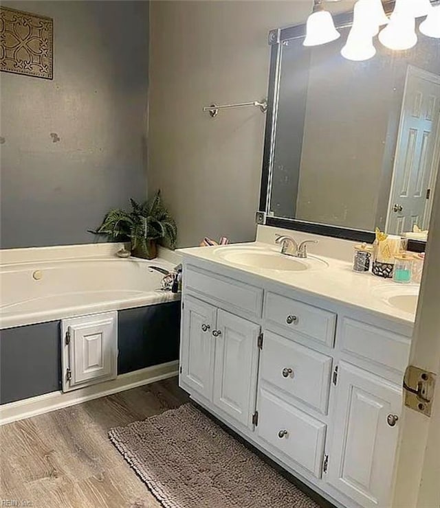 full bath with a garden tub, double vanity, wood finished floors, and a sink