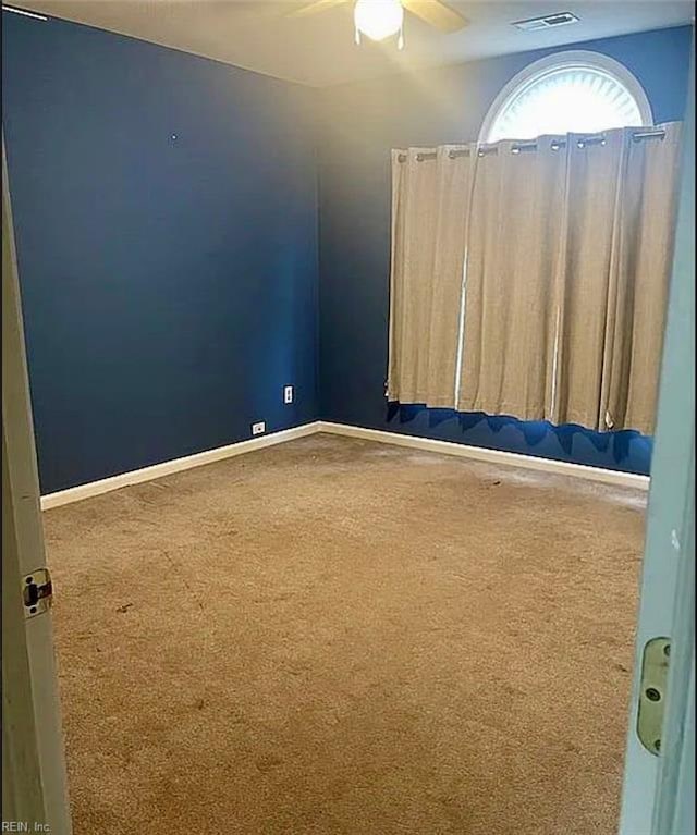 empty room with carpet floors, baseboards, visible vents, and a ceiling fan