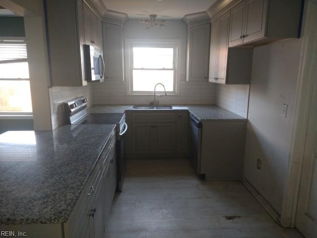 kitchen with light wood finished floors, tasteful backsplash, stainless steel appliances, stone counters, and a sink