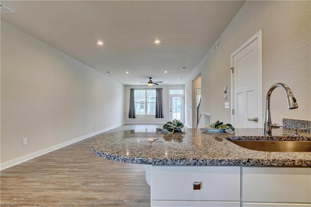 kitchen with a sink, stone counters, visible vents, and light wood-style flooring