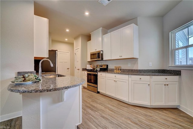 kitchen with light wood-style flooring, stainless steel appliances, a peninsula, white cabinets, and baseboards