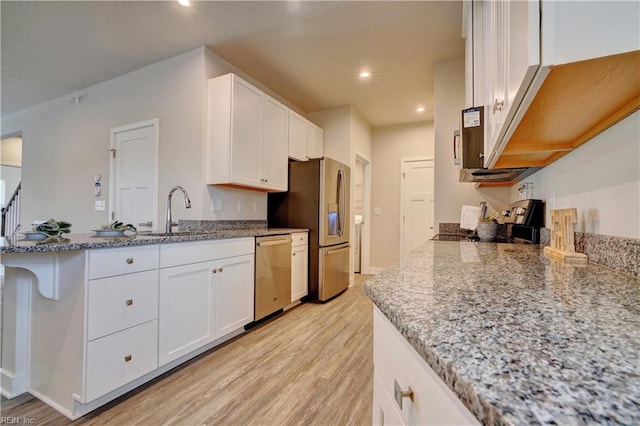 kitchen with light wood finished floors, a peninsula, a sink, appliances with stainless steel finishes, and white cabinetry