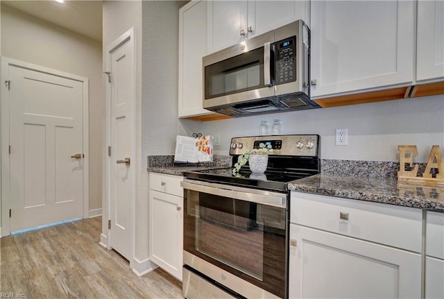 kitchen with white cabinetry, dark stone countertops, light wood-style floors, and stainless steel appliances