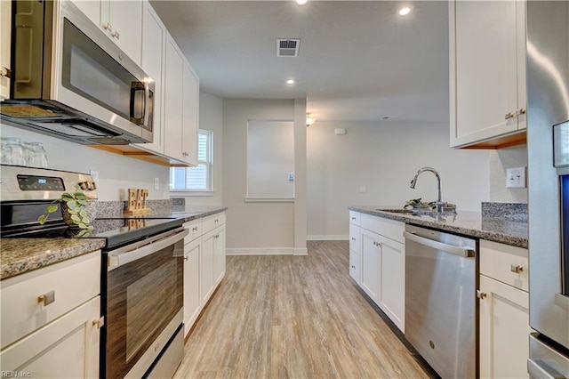 kitchen with visible vents, dark stone counters, appliances with stainless steel finishes, light wood-style floors, and a sink