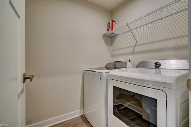 clothes washing area with wood finished floors, baseboards, laundry area, a textured wall, and independent washer and dryer