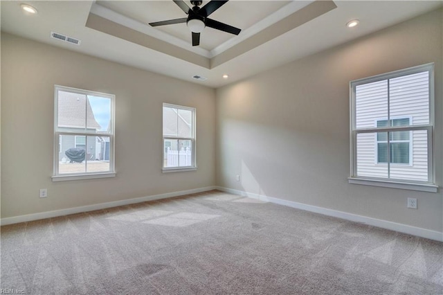 empty room featuring a tray ceiling, baseboards, visible vents, and light carpet