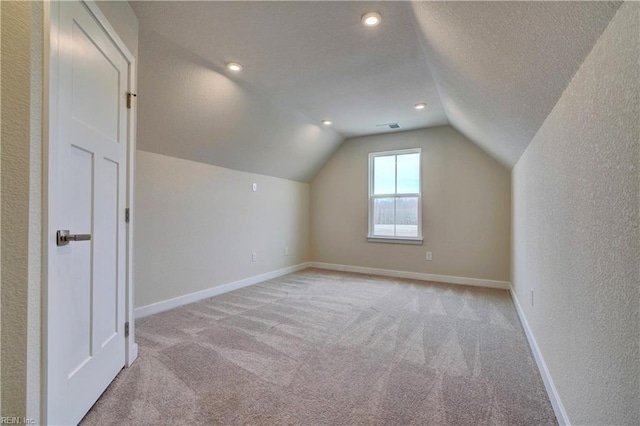 additional living space with baseboards, light colored carpet, a textured ceiling, and lofted ceiling