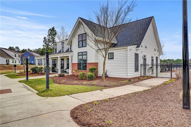 view of front of home with a gate, fence, roof with shingles, a front lawn, and brick siding