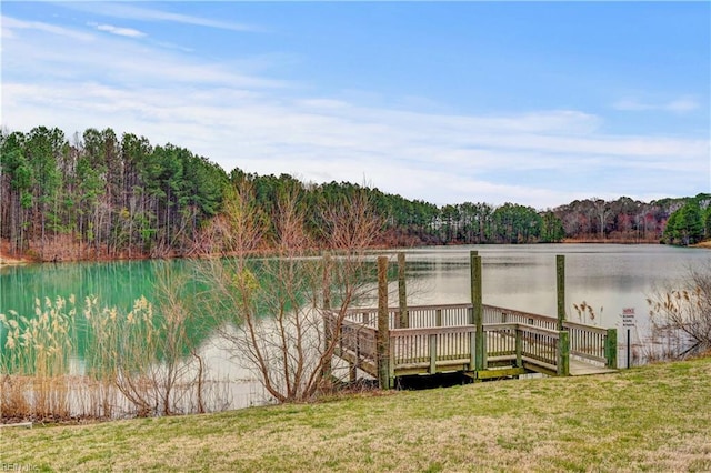 view of dock with a wooded view, a yard, and a water view