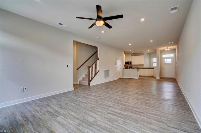 unfurnished living room with stairway, visible vents, baseboards, and light wood-style floors