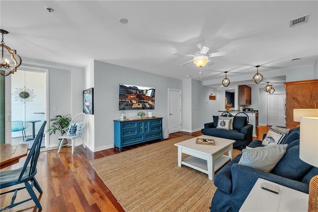 living room featuring ceiling fan with notable chandelier, wood finished floors, visible vents, and baseboards