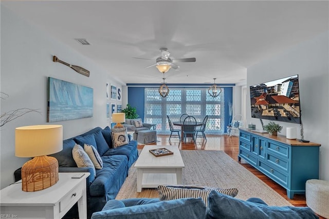 living room featuring dark wood-style flooring, visible vents, and ceiling fan with notable chandelier